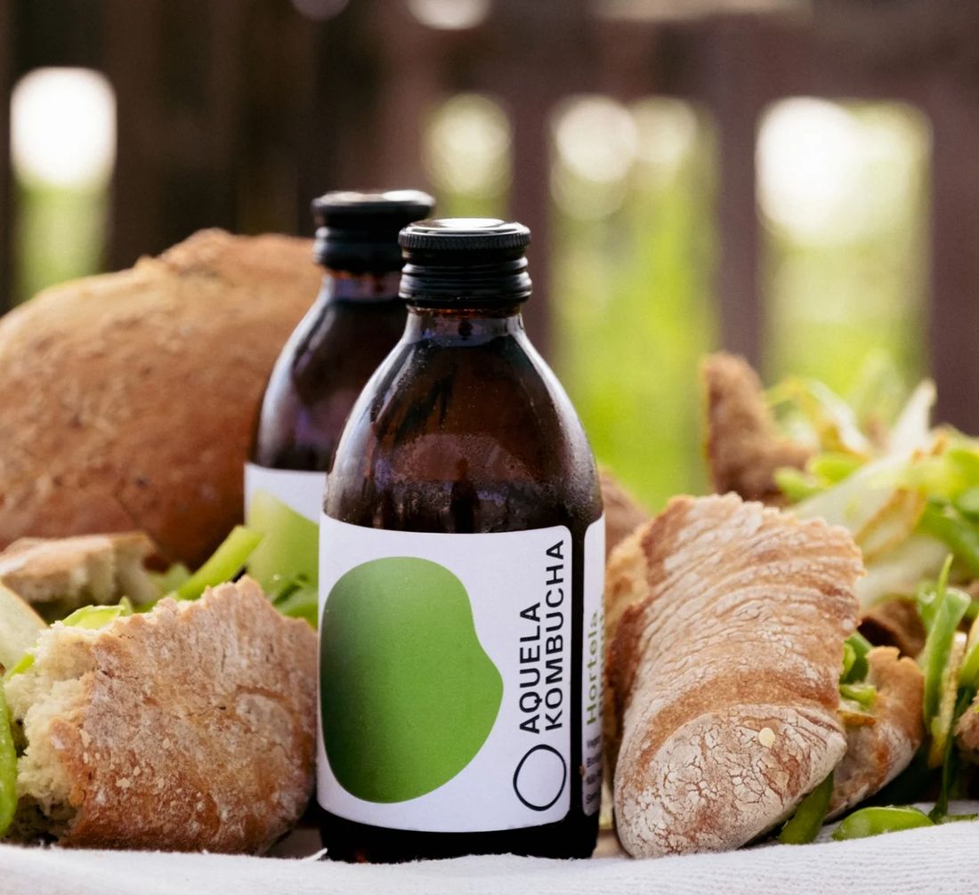 Duas garrafas de Aquela Kombucha Hortelã-Pimenta numa mesa com pão