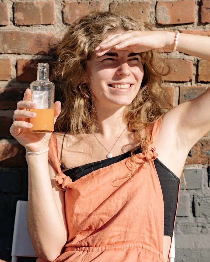 Mulher sorridente ao sol com uma garrafa de vidro com bebida dourada