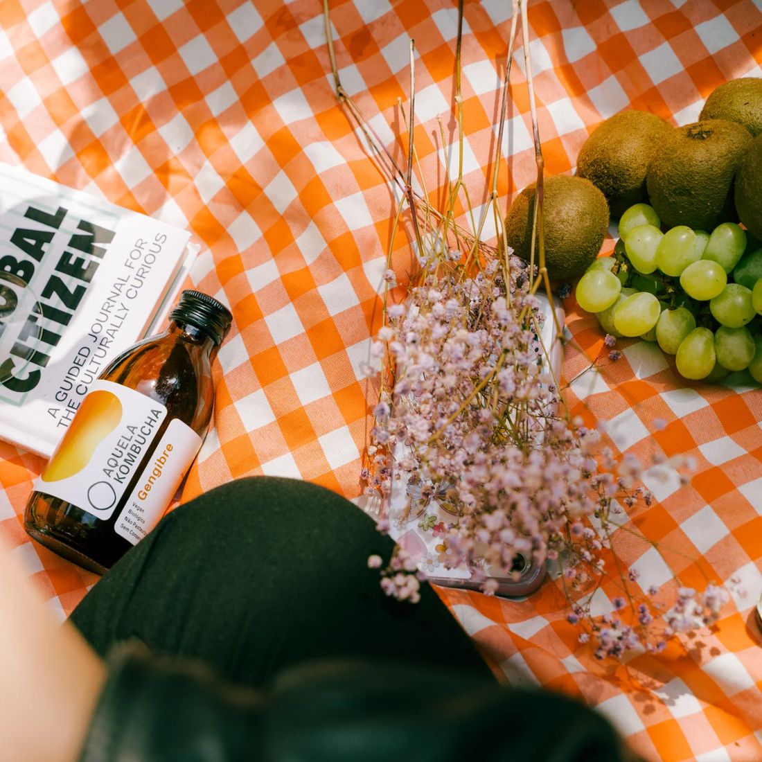 Garrafa de Aquela Kombucha numa toalha de piquenique aos quadrados laranja
